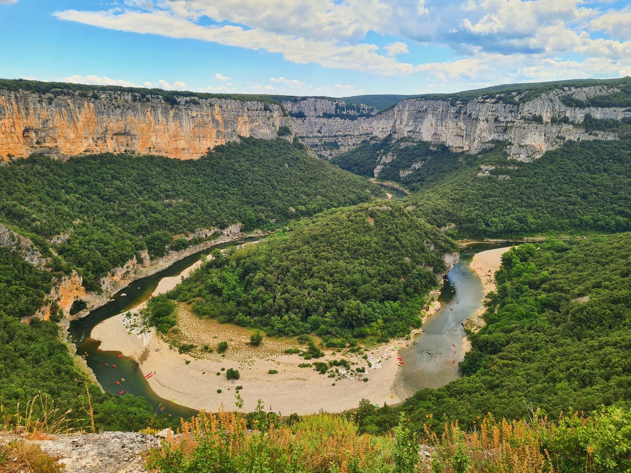 Rivière sinueuse encadrée de hautes falaises calcaires grises et ocre avec végétation méditerranéenne