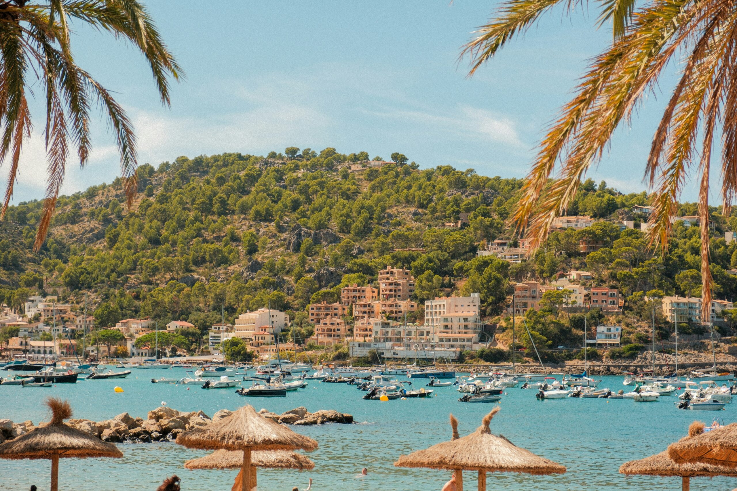 Baie méditerranéenne avec bateaux au mouillage, palmiers et village en bord de mer.